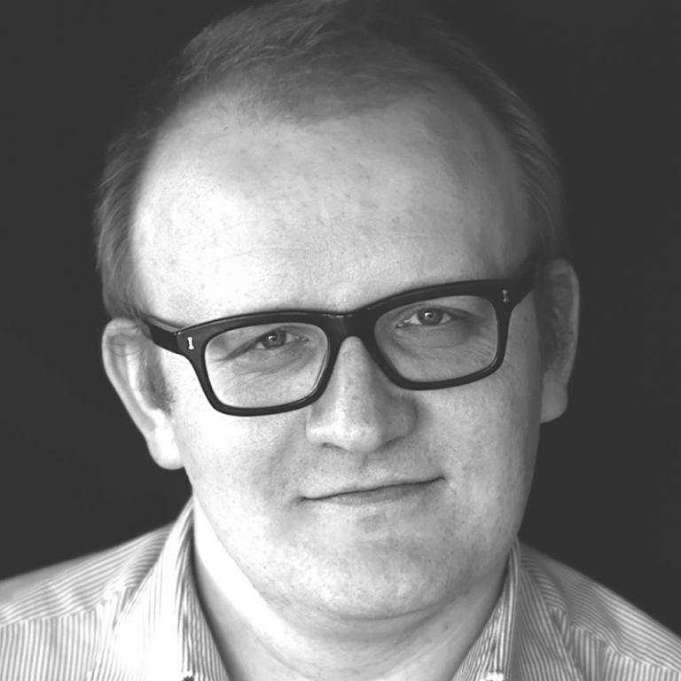Czarno-białe zdjęcie - portret dr Marcina Gody (młody mężczyzna w okularach, uśmiech na twarzy)