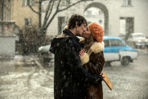 Młody chłopak i dziewczyna całujący się na ulicy. Pada śnieg. W tle brama budynku i samochody z lat 70tych,