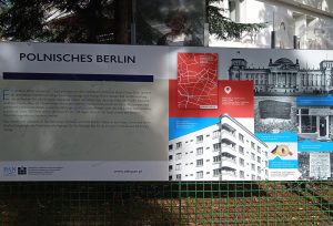 Plansza wystawiennicza wisząca na siatce ogrodowej. W lewej części  planszy nagłówek "Polnisches Berlin" a pod nim tekst. Po prawej stronie planszy mapa z ulicami, zdjęcia budynków, tablic pamiątkowych z opisem tekstowym. 