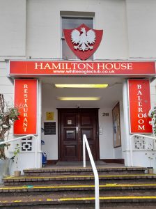 Fasada budynku, do którego prowadzą schody. Nad wejściem godło z polskim orłem i napis "Hamilton House, www.whiteeagleclub.co.uk", Po bokach drzwi napisy "Restaurant" i "Ballroom"